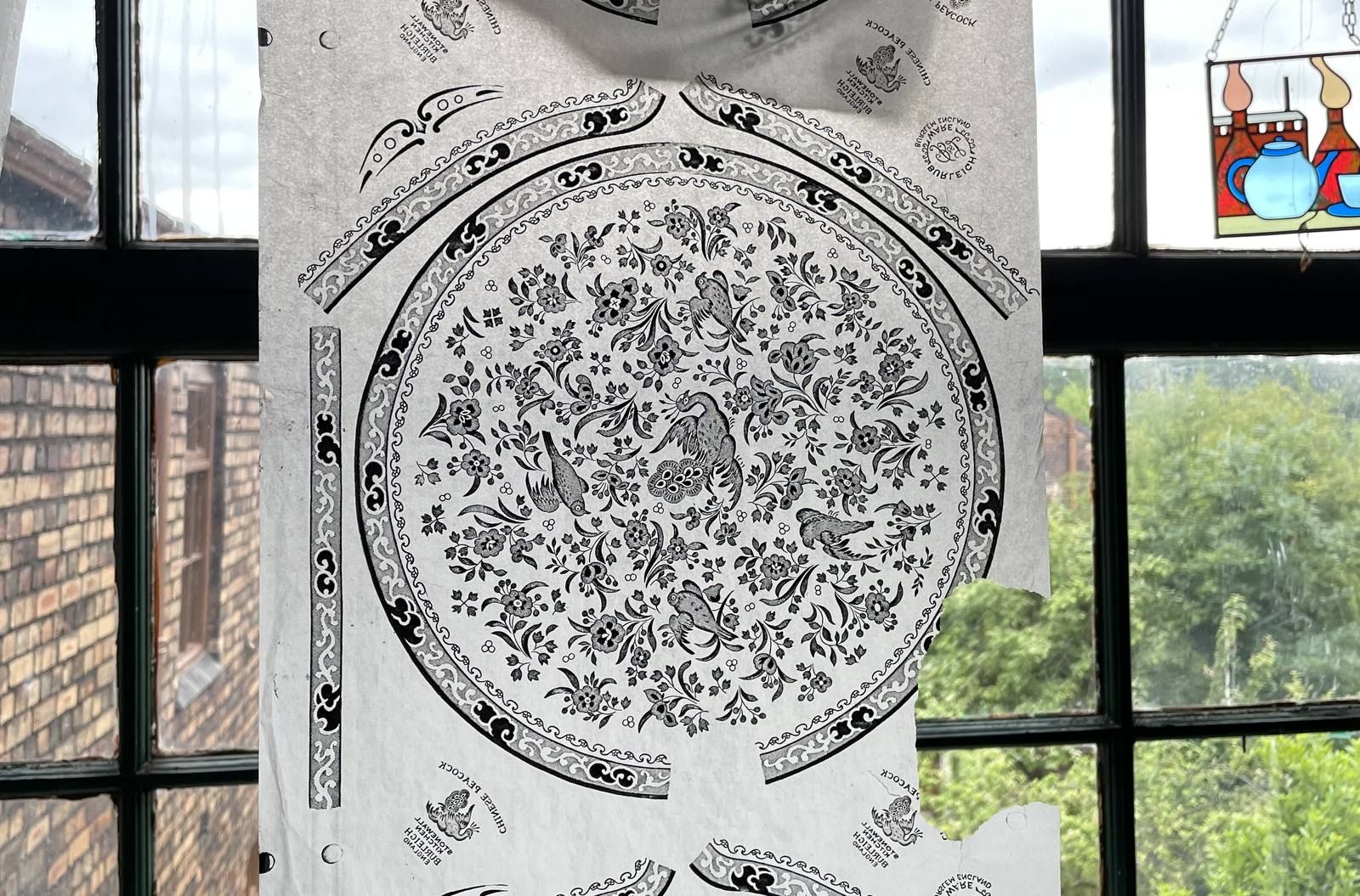 A Burleigh transfer-print pattern on tissue hanging in front of a factory window at Middleport Pottery.