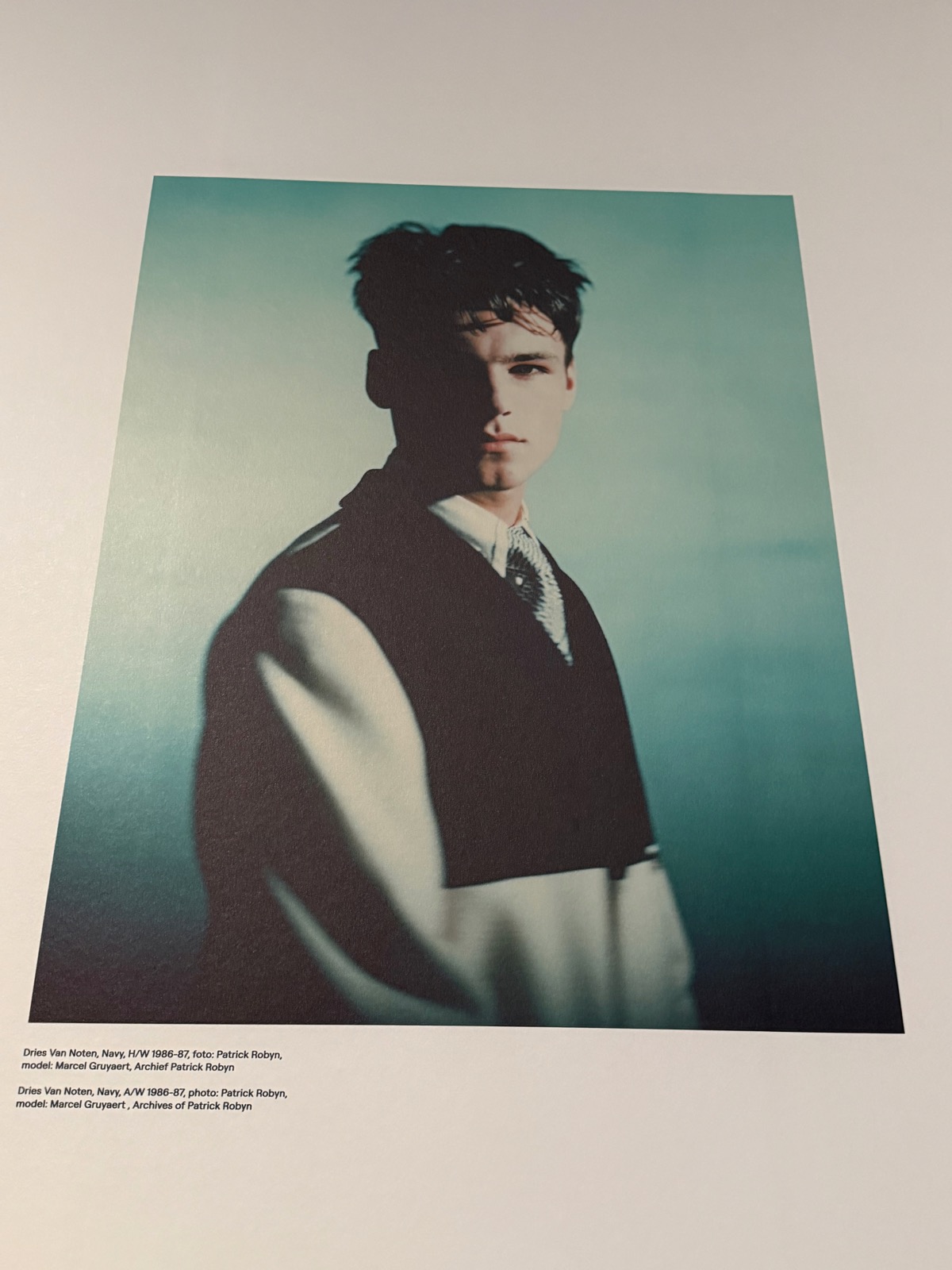 Archive press photograph of a model in Dries Van Noten Navy, A/W 1986-87, against a teal ground.