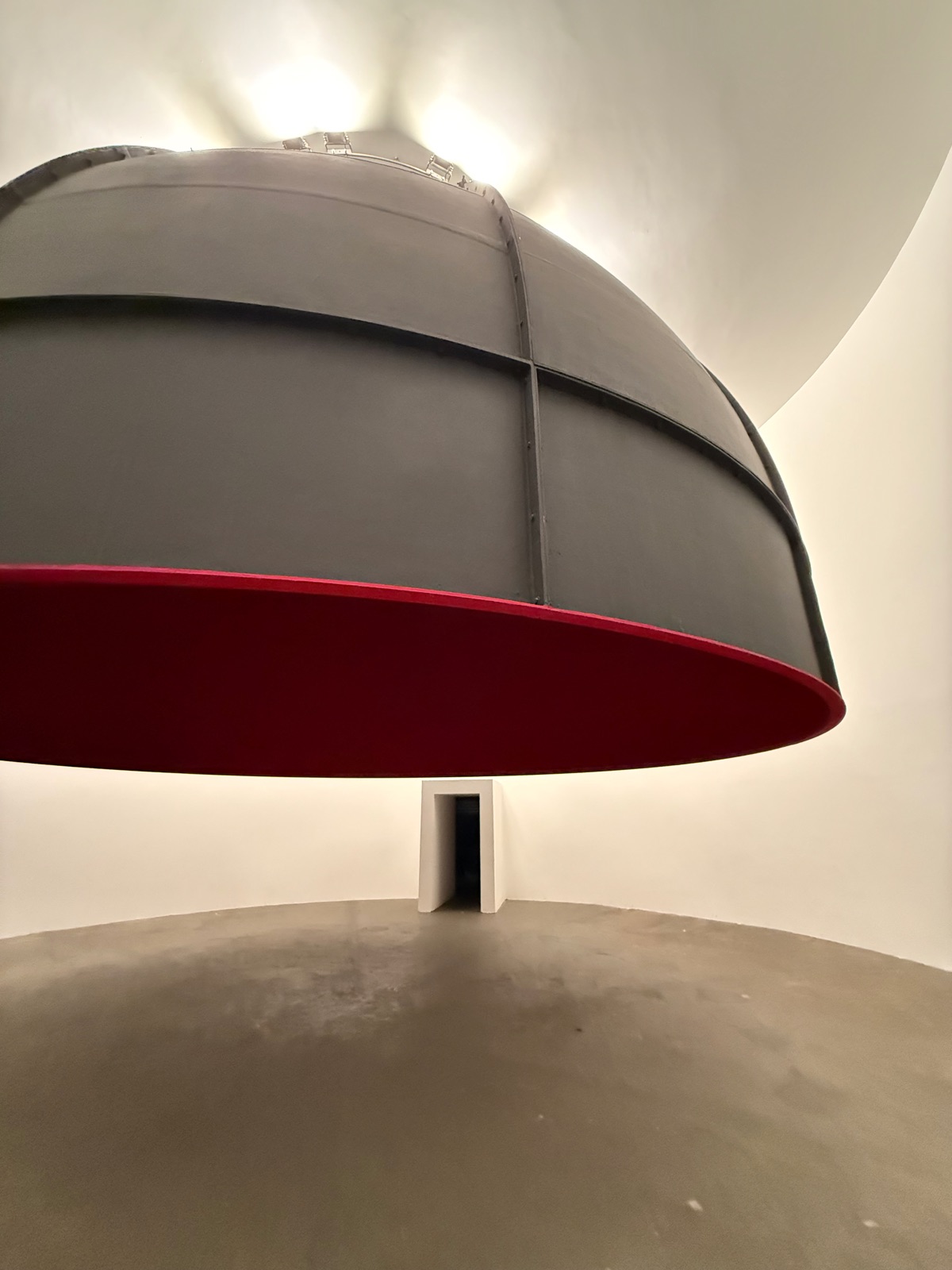 Anish Kapoor's suspended dome seen from below, grey on the outside and deep red within, inside the round building.