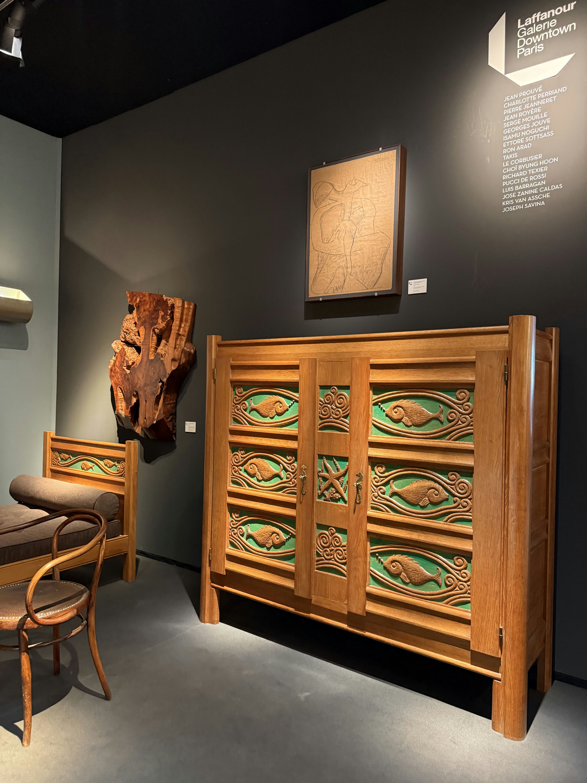 Joseph Savina and Le Corbusier's carved-oak fish cabinet on the Laffanour / Galerie Downtown stand at PAD Paris 2026, a carved-back chair to its left and the gallery's artist list on the wall.