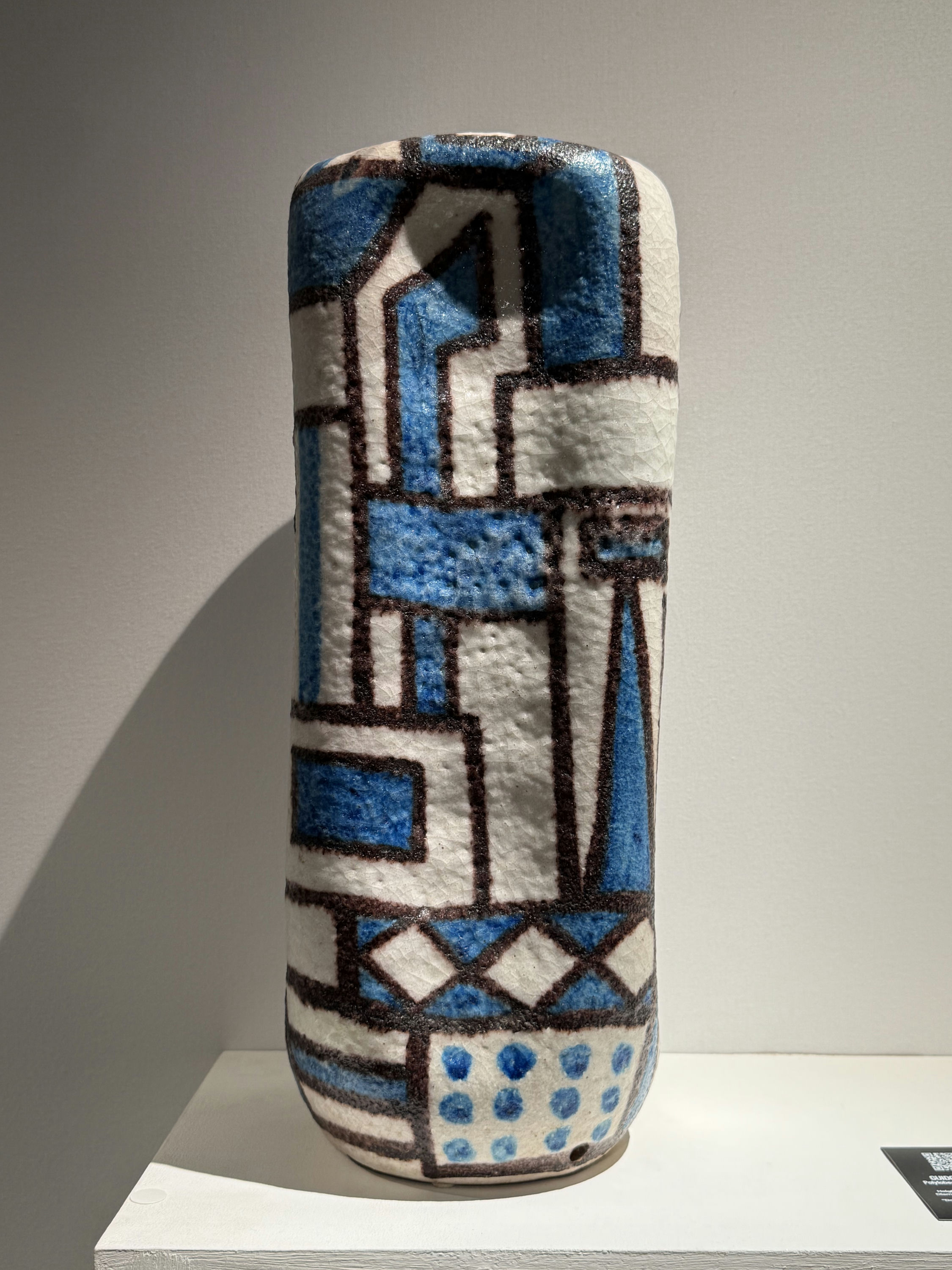 A tall enamelled ceramic vessel by Guido Gambone, blue and black geometric glaze over a white ground, on a plinth at Gaïa & Romeo.