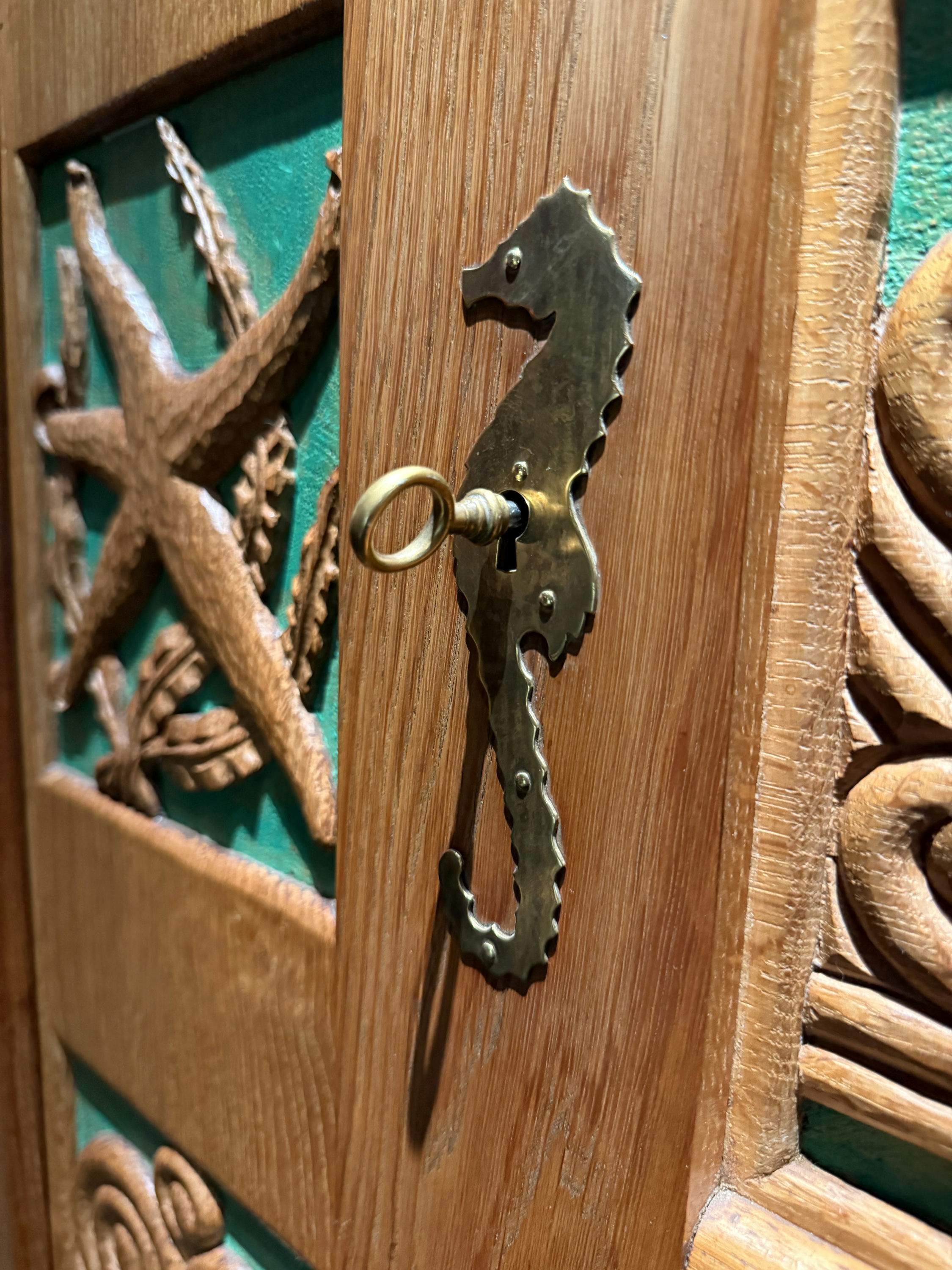 A brass escutcheon in the shape of a seahorse set into the carved oak, a small key in the lock, a carved starfish panel beside it.