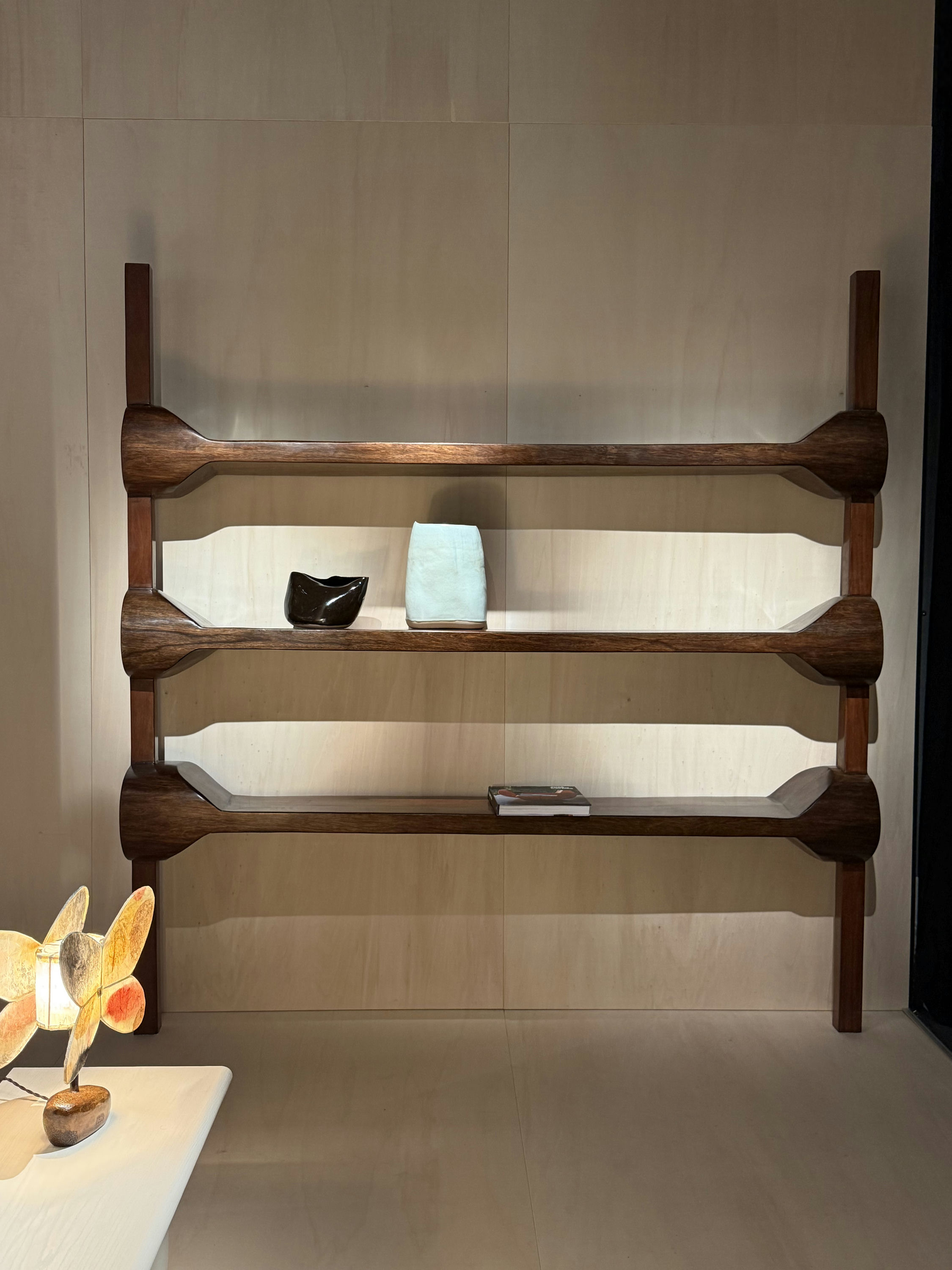 A wall-mounted shelving unit by José Zanine Caldas in dark tropical hardwood, the brackets carved from solid timber, a small ceramic and a book on the shelves.