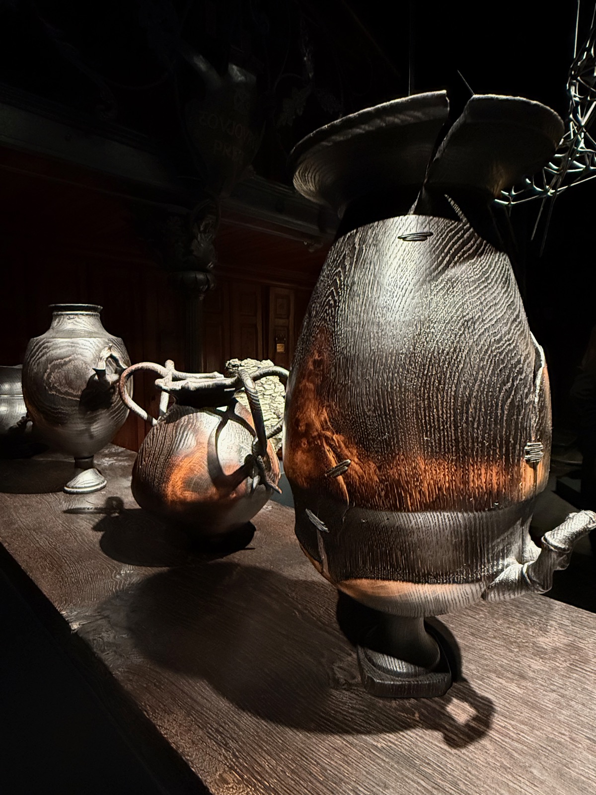 Charred, scorched turned-wood vessels grouped on a dark table under dramatic light.