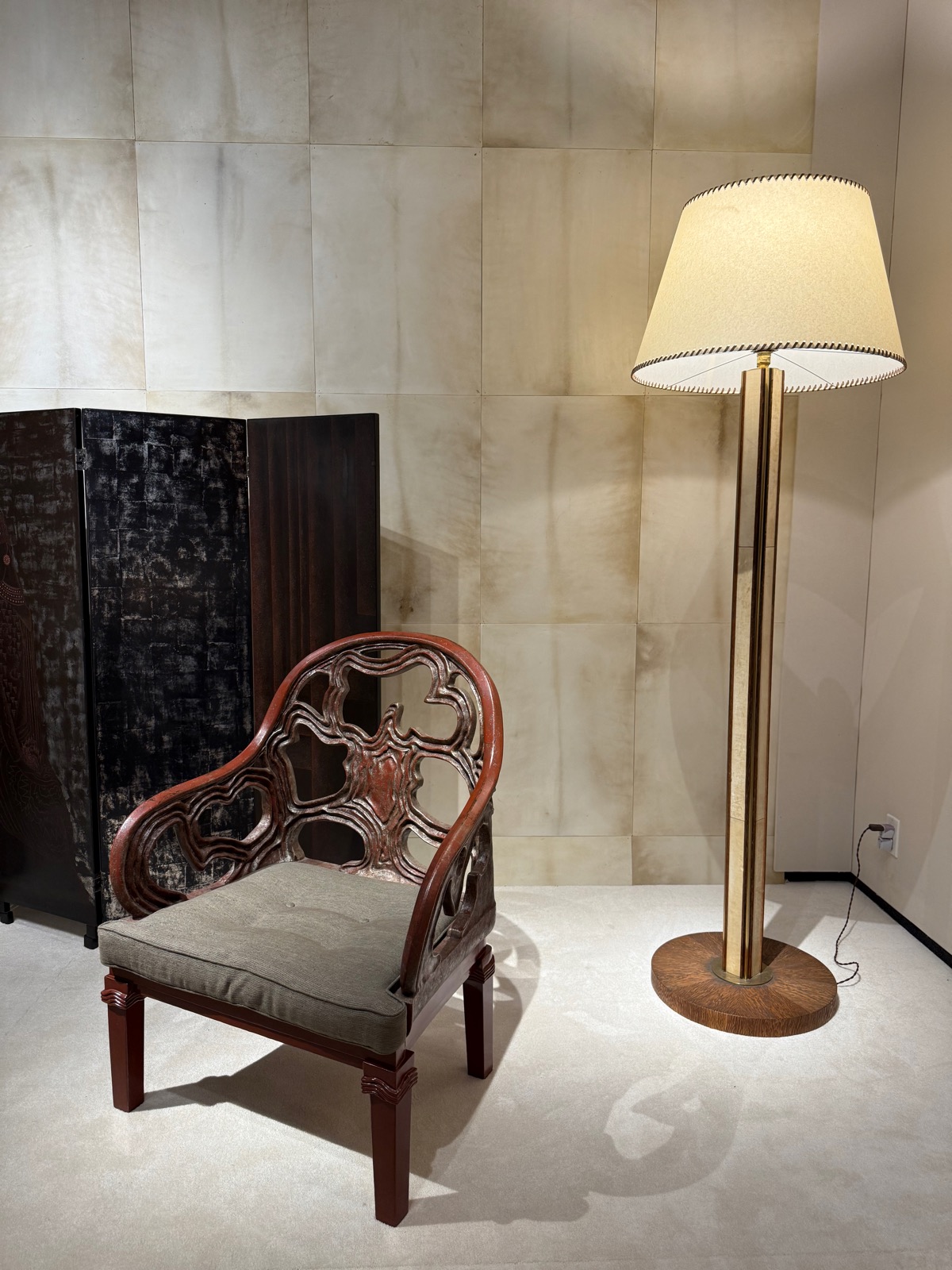 A parchment-walled Art Deco booth with a carved wooden armchair, a dark lacquer screen and a brass floor lamp.