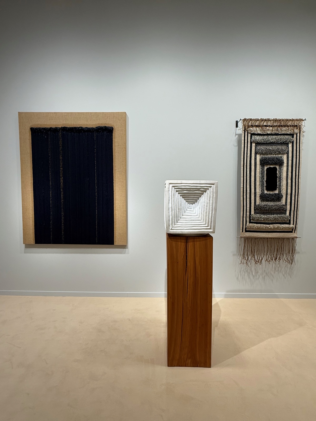 The Sarah Myerscough stand: a dark fibre-art panel, a white carved square vessel on a wooden plinth, and a woven textile hanging.