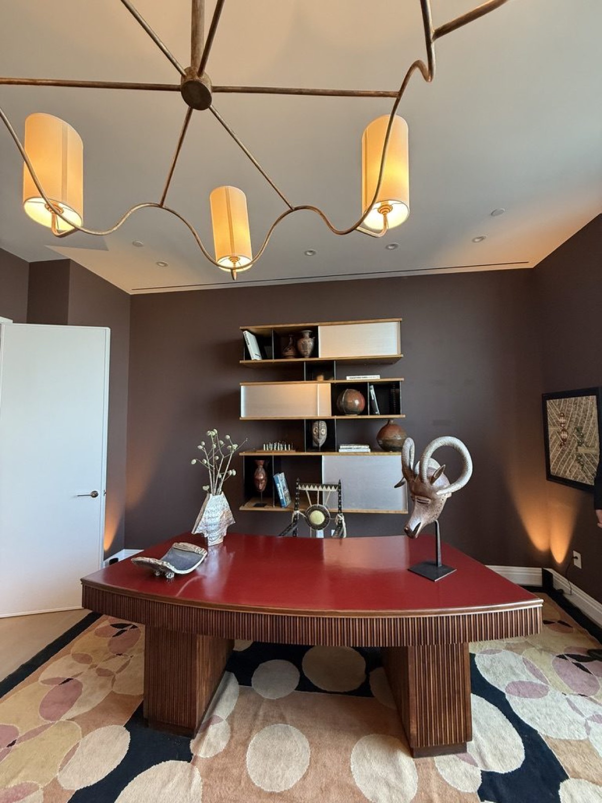 An Art Deco red-leather desk beneath a sinuous brass chandelier in the study.