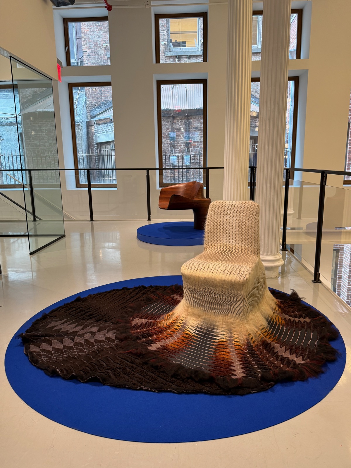 A chair whose woollen seat cascades into a wide woven fan across a cobalt-blue floor disc.
