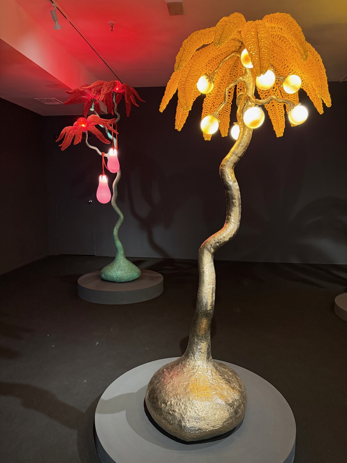 Crocheted, illuminated tree-lamp sculptures glowing orange and red in a darkened room.