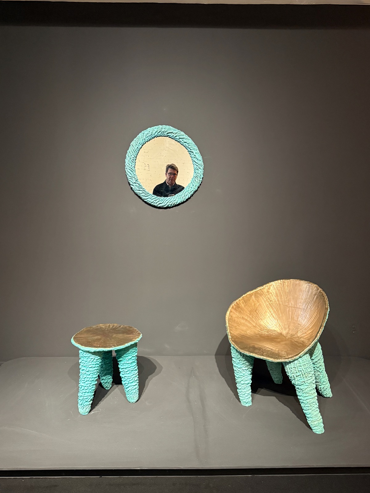 A cast-bronze chair with rough turquoise legs and a polished gold seat, beside a matching turquoise mirror, at R & Company.