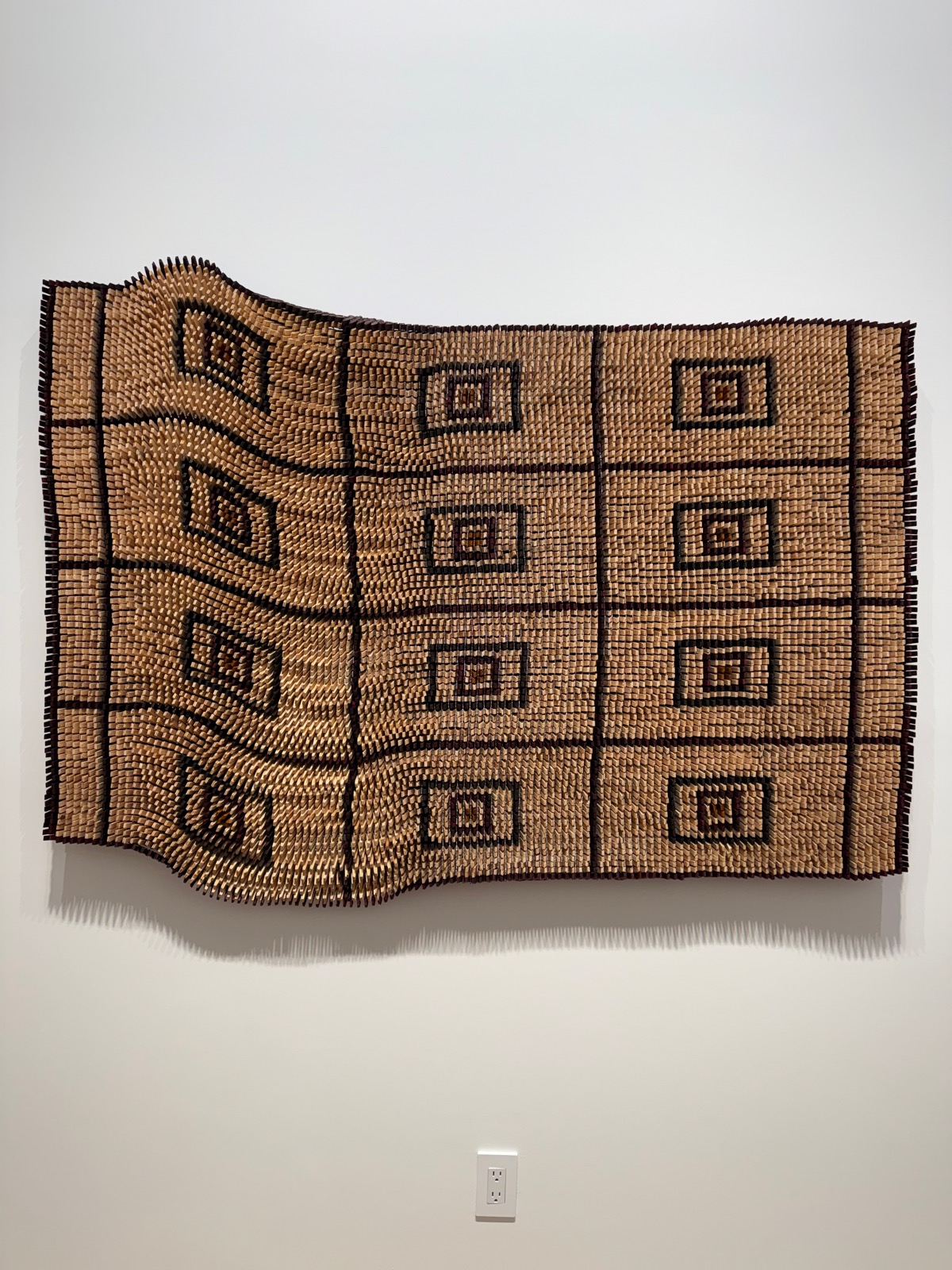 A large wall hanging of thousands of wooden clothes pegs arranged in a grid that reads like a woven rug.