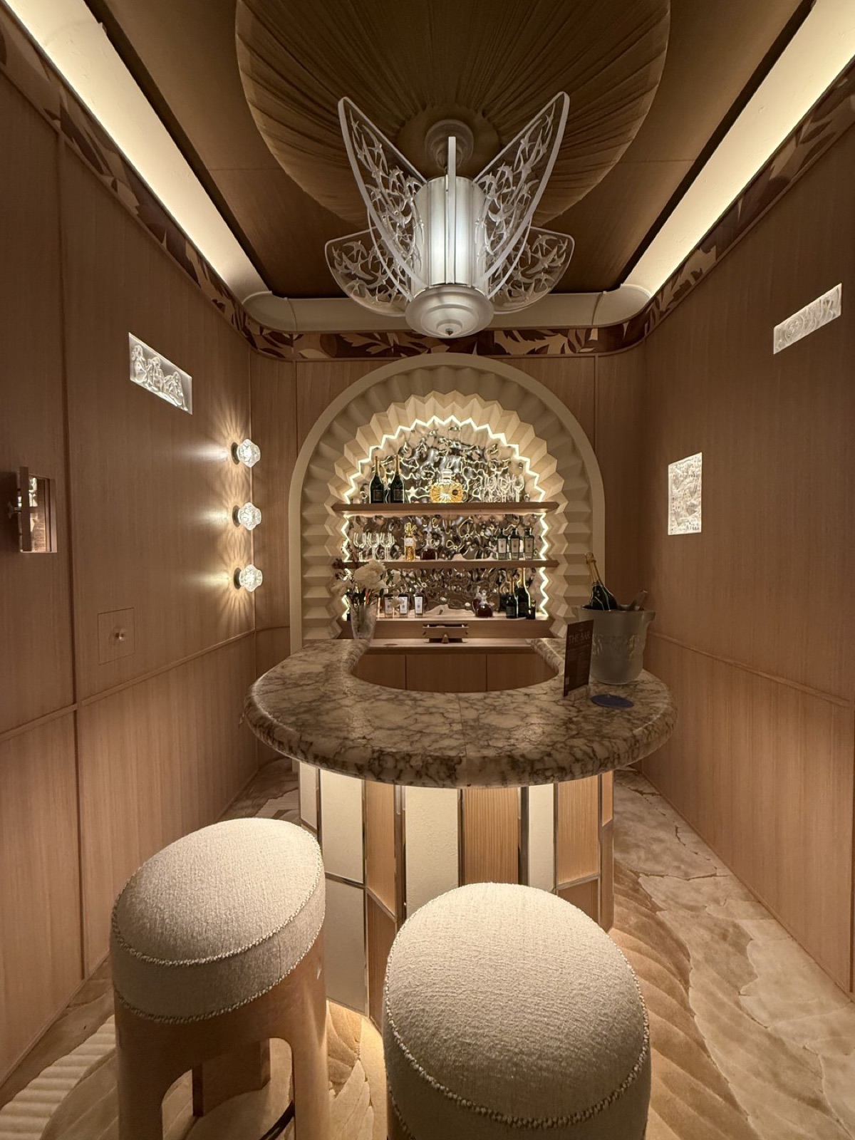Charu Gandhi's Lalique Home Bar for Elicyon: a curved alabaster bar under a Lalique 'Swallows' crystal chandelier, the walls lined in crystal.